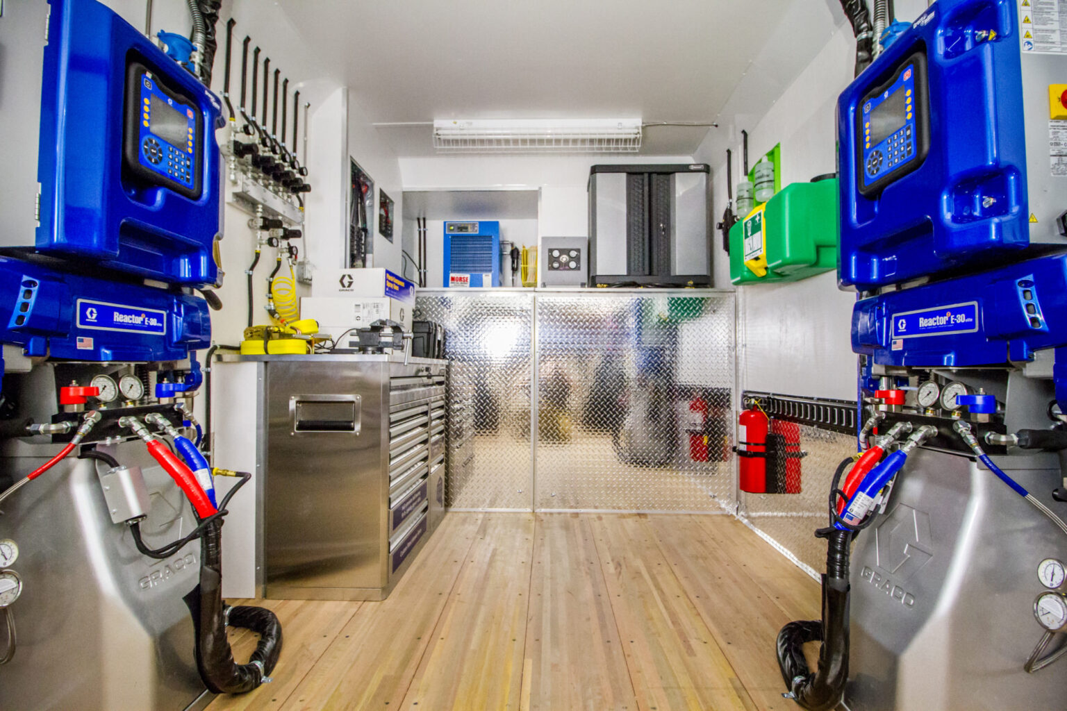 Interior of a spray foam rig trailer with two proportioners, hose racks, a tool chest and diamond plate walls